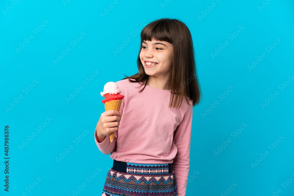 Little girl with a cornet ice cream isolated on blue background looking to the side and smiling Little girl with a cornet ice cream isolated on blue background looking to the side and smiling