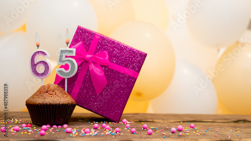 Happy birthday with pink gift box for 65 year old woman. Beautiful birthday card with cupcake and burning candle number sixty five.