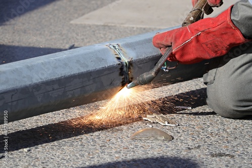 Φωτογραφία Male hand in red glove cutting the overturned lamppost with a blowtorch