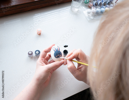 woman paints an Easter egg with paints. Easter bunny drawing on a white egg photo