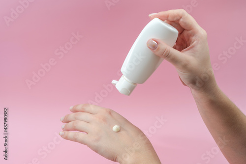 Young hands squeezing cream from tube on pink background. For beauty or medicine products
