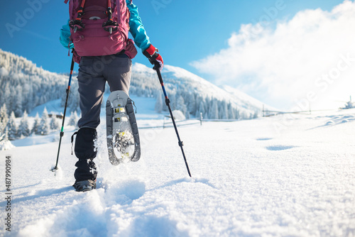 A woman with a backpack in snowshoes climbs a snowy mountain photo