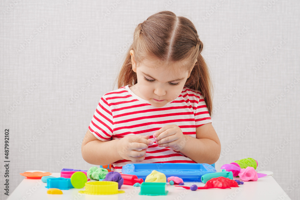 little girl in striped T-shirt sculpts figures from plasticine, play dough, developing creative activities little girl in striped T-shirt sculpts figures from plasticine, play dough, developing creative activities