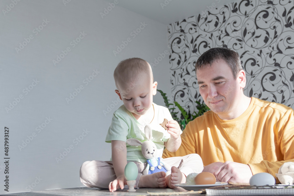 Naklejka premium A dad celebrates Easter with his young son. They beat eggs, eat eggs and have breakfast. Dad teaches the child.
