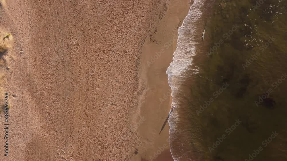 Aerial top down view of person walking on the beach at Punta del Este Uruguay. Wave and foam at sunrise.