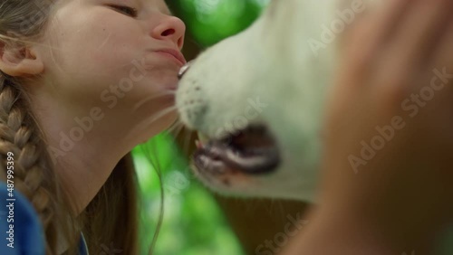 Portrait of chewing girl caressing dog closeup. Pet lick cute face on picnic. photo