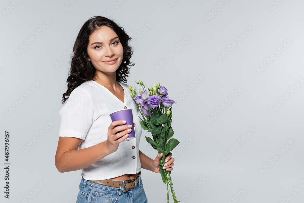 pleased young woman holding bouquet of purple flowers and paper cup isolated on grey. pleased young woman holding bouquet of purple flowers and paper cup isolated on grey.