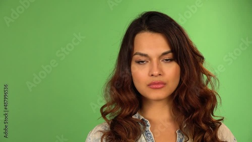 A young beautiful Caucasian woman looks seriously at the camera - closeup - green screen background