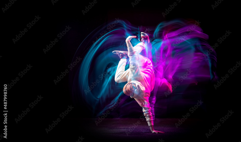 Dynamic portrait of young flexible sportive boy dancing hip-hop or breakdance in white outfit on dark background in mixed pink neon light. Sport, art, action, moves Dynamic portrait of young flexible sportive boy dancing hip-hop or breakdance in white outfit on dark background in mixed pink neon light. Sport, art, action, moves