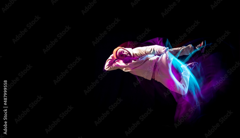 Obraz premium Dynamic portrait of young flexible sportive boy dancing hip-hop or breakdance in white outfit on dark background in mixed pink neon light. Sport, art, action, moves