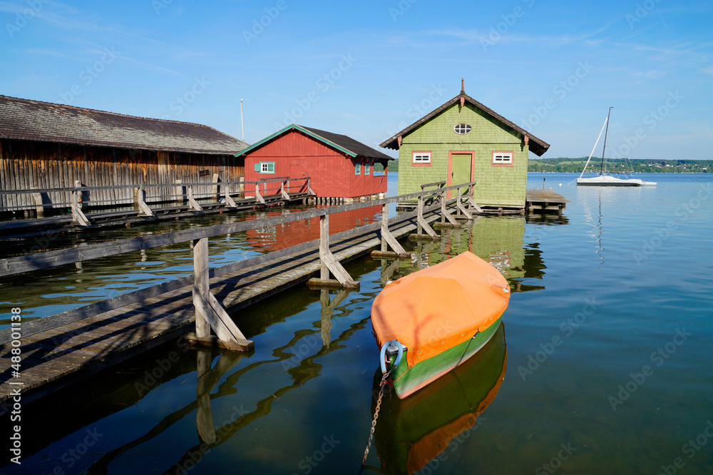 Obraz premium a long wooden pier leading to the colorful boat houses on lake Ammersee in the German fishing village Schondorf (Germany) 