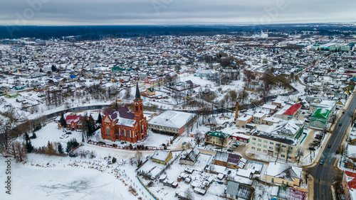 Aerial view of red catholic church and small town in winter. Idyllic landscape with church, houses, river and riverbank. © kalyanby