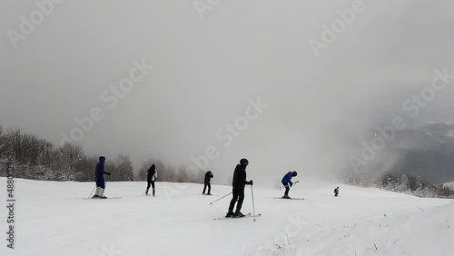 Skiers in bad weather and snowstorm quickly descend the slope of the mountain, before them opens a breathtaking panorama of the mountain ranges surrounding the slope