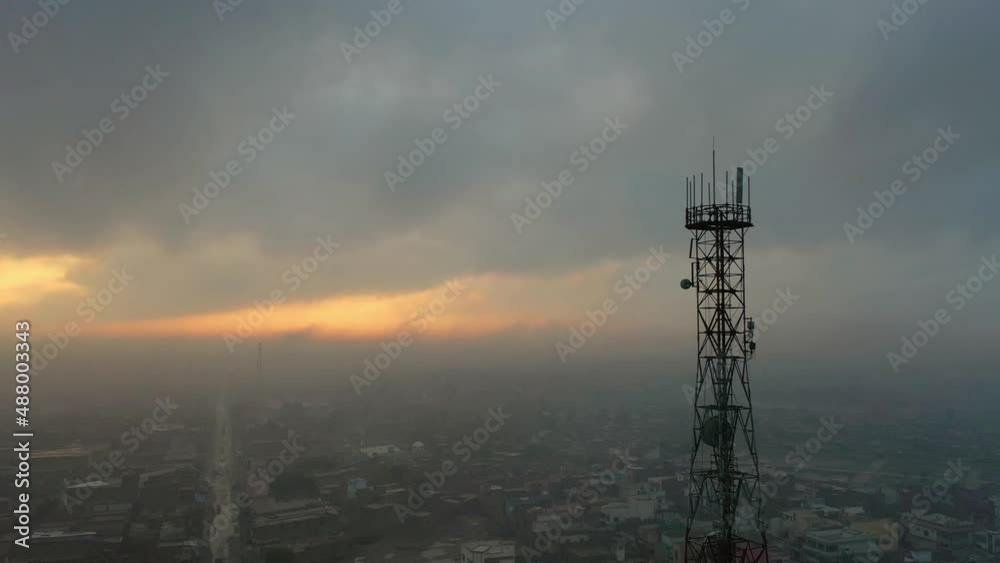 Aerial View Of Telecommunications Tower On Cloudy Overcast Day With Yellow Sun Light In Distance Over Moro City Sindh. Parallax Aerial View Of Telecommunications Tower On Cloudy Overcast Day With Yellow Sun Light In Distance Over Moro City Sindh. Parallax