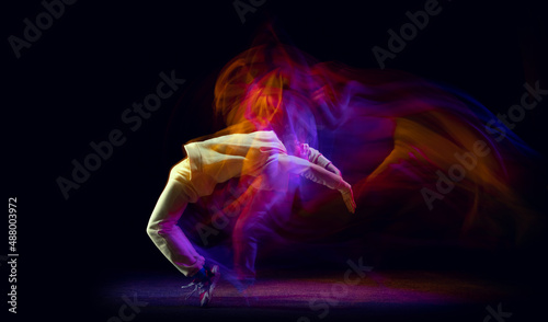 Solo dance. Young flexible sportive man dancing hip-hop or breakdance in white outfit on dark background in mixed yellow neon light. Beauty, sport, youth, action, moves