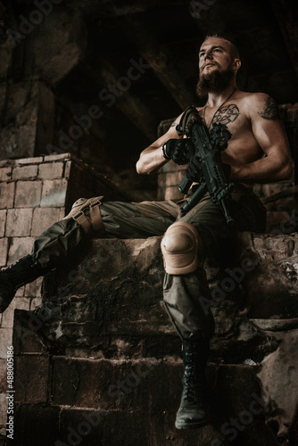 a soldier in military clothes poses in an abandoned building with a gun in his hands