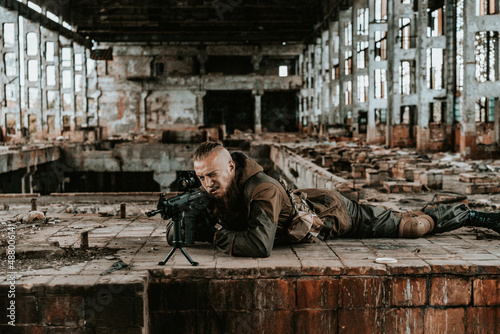 a male military soldier in an abandoned building with a gun poses, shoots and takes aim