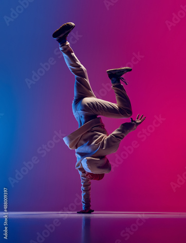 Studio shot of young flexible sportive man dancing breakdance in white outfit on gradient pink blue background. Concept of action, art, beauty, sport, youth photo