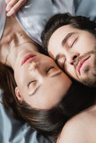 top view of young woman and man with closed eyes lying on bed.