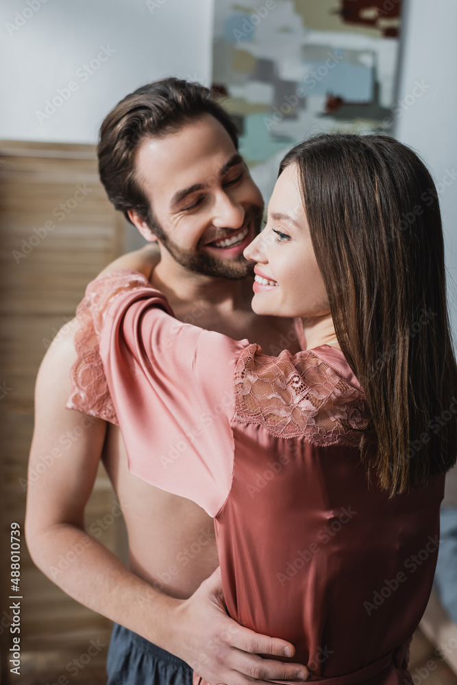Naklejka premium happy young woman in pink silk robe hugging cheerful man.