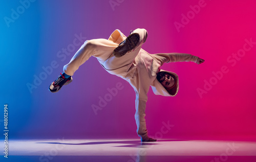 Studio shot of young flexible sportive man dancing breakdance in white outfit on gradient pink blue background. Concept of action, art, beauty, sport, youth photo
