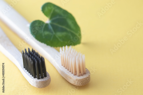 Bamboo toothbrushes with beige and black bristles lie on a yellow background. Close-up.