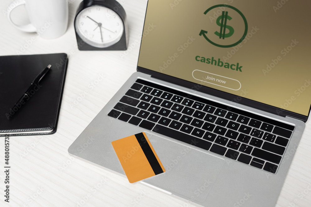 credit card on laptop with cashback on screen near notebook and cup on white desk. credit card on laptop with cashback on screen near notebook and cup on white desk.