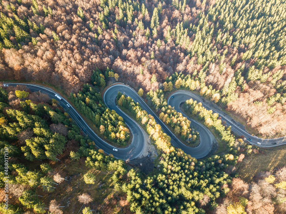 Winding road from high mountain pass, in summer time. Aerial view of a green forest and an empty road traffic