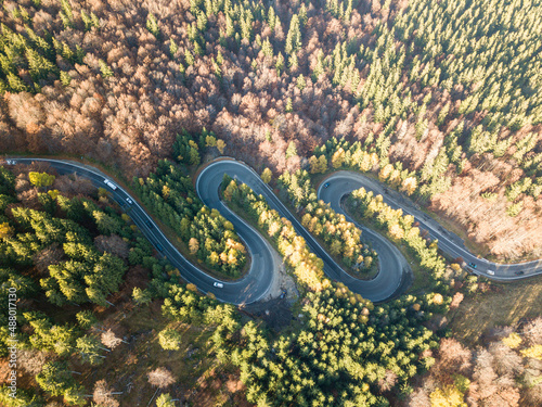Winding road from high mountain pass, in summer time. Aerial view of a green forest and an empty road traffic