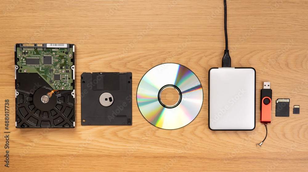 Fototapeta premium Data storage devices such as CDs, hard drives, pen drives and other, top view on a wooden background