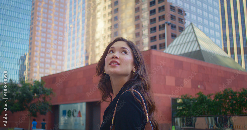 Brunette woman exploring cityscape. Asian girl looking up on high buildings.
