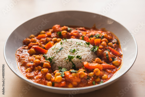vegan chickpeas curry. close up of fresh vegetarian indian curry known as chana masala with basmati rice and coriander leaves on table with soft natural light