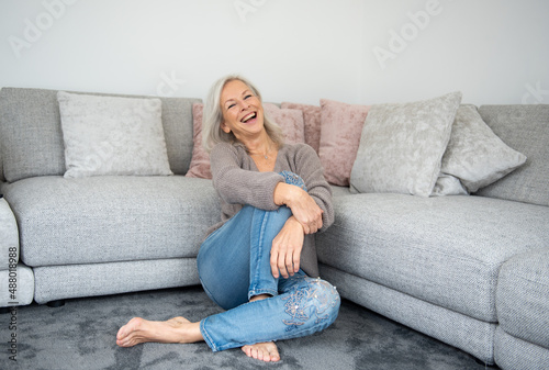 bellissima donna over sessanta con jeans seduta per terra a gambe incrociate che sorride verso l'obiettivo piena di gioia di vivere  photo