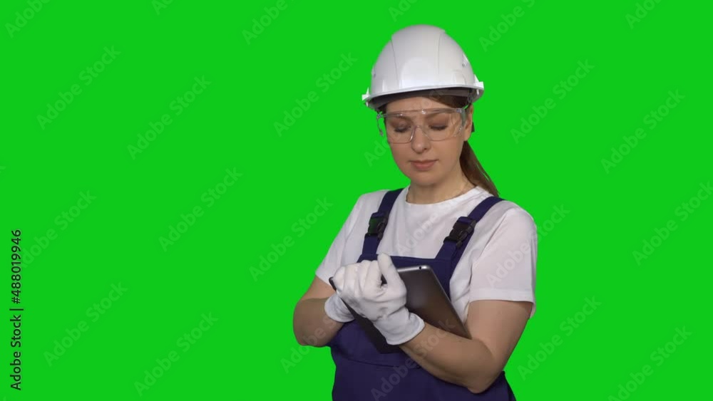 Woman builder in blue overalls and white hard hat helmet with tablet device. Woman builder in blue overalls and white hard hat helmet with tablet device.