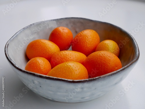 Close up of kumquats, cumquats, in grey ceramic bowl against white background.