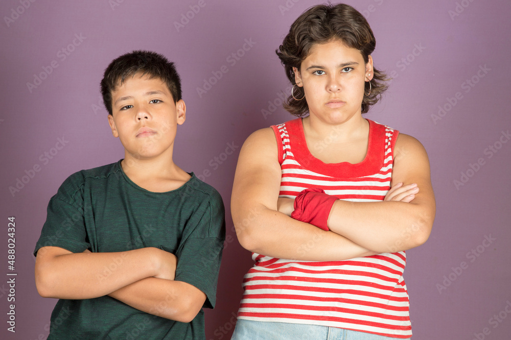 Young latin brother and sister wearing casual clothes standing back to back with arms crossed and looking at camera with serious and negative mood on purple background. Wrong behavior concept Young latin brother and sister wearing casual clothes standing back to back with arms crossed and looking at camera with serious and negative mood on purple background. Wrong behavior concept