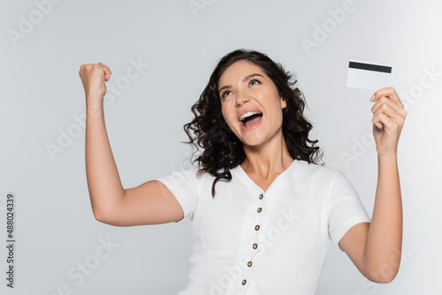 excited young woman holding credit card with cashback and rejoicing isolated on grey.