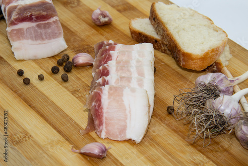 Ukrainian traditional food concept with white bread. Ukrainian raw lard with peppercorn and garlic, knife, slices of salo lying on wooden cutting board.