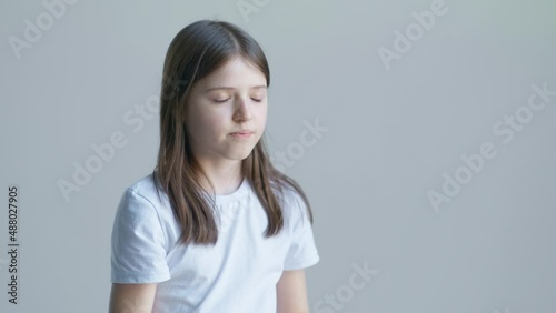 A teenager blonde girl in a white T-shirt and holds a pill in her palm and swallows against the background of a white wall