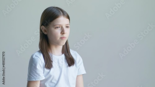 A teenager blonde girl in a white T-shirt and holds a pill in her palm and swallows against the background of a white wall