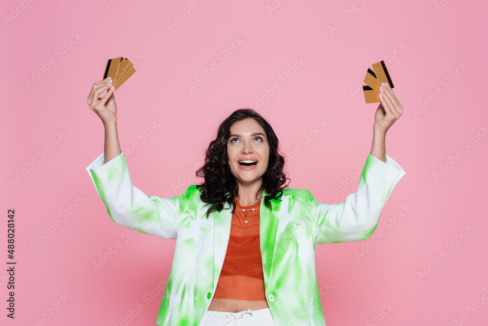amazed young woman in green tie dye blazer looking at credit cards and smiling isolated on pink. amazed young woman in green tie dye blazer looking at credit cards and smiling isolated on pink.