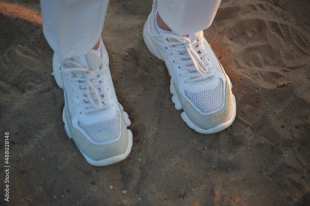 White sneakers, shoes and white pants, a girl standing on the sand during sunset
