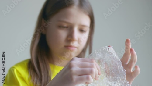 A blonde teenager girl in a yellow T-shirt bursts bubble wrap and is bored