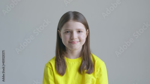 Blonde teenager girl in a yellow T-shirt smile against the background of a white wall