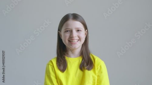 Blonde teenager girl in a yellow T-shirt laughs against the background of a white wall