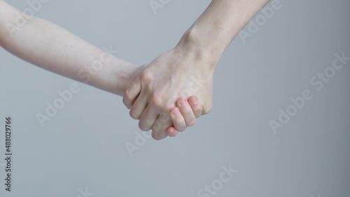Woman and child join hands and hold in front of the background of a white wall
