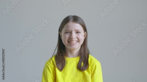 Blonde teenager girl in a yellow T-shirt laughs against the background of a white wall