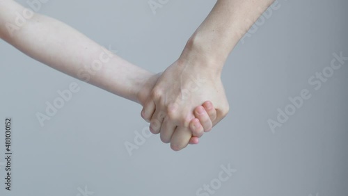 Woman and child join hands and hold in front of the background of a white wall