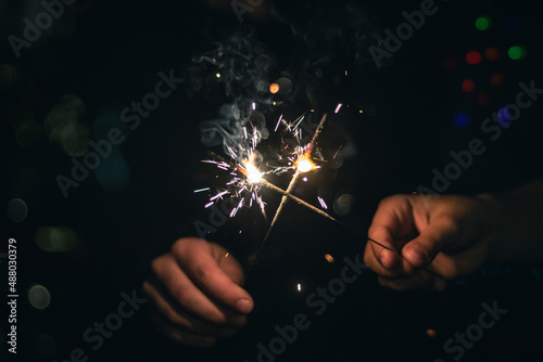 Kids holding burning party sparklers. Dark bokeh background, close up, celebration concept. 