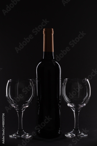 Wine bottle and two glasses positioned symmetrically against a solid black backdrop, highlighting minimalistic design.